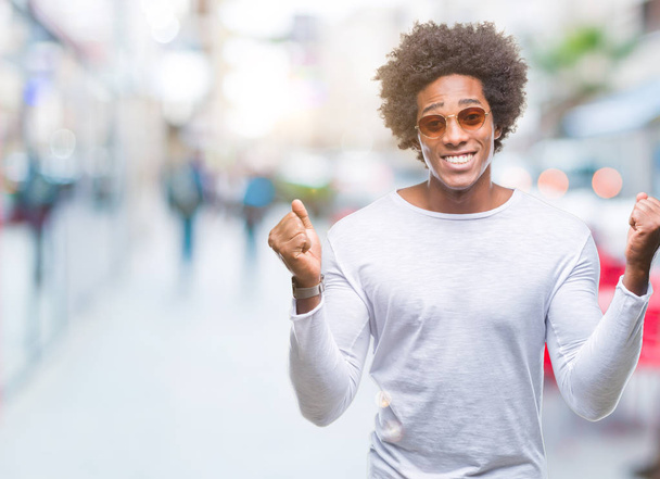Hombre afroamericano con gafas de sol sobre fondo aislado celebrando sorprendido y sorprendido por el éxito con los brazos levantados y los ojos abiertos. Concepto ganador
. - Foto, imagen
