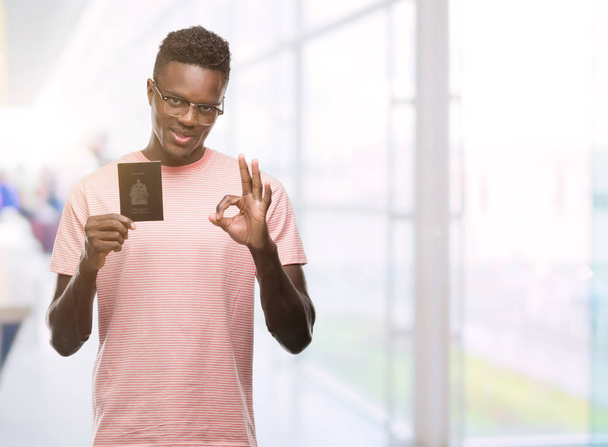 Jonge Afro-Amerikaanse man met Canadese paspoort doen ok teken met vingers, uitstekende symbool - Foto, afbeelding