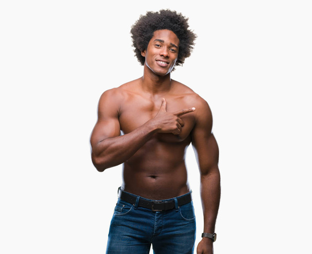 Hombre afroamericano sin camisa mostrando el cuerpo desnudo sobre fondo aislado alegre con una sonrisa de la cara señalando con la mano y el dedo hacia el lado con expresión feliz y natural en la cara mirando a la cámara
. - Foto, imagen