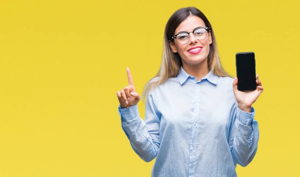 Young beautiful business woman showing blank screen of smartphone over isolated background very happy pointing with hand and finger to the side - Photo, image