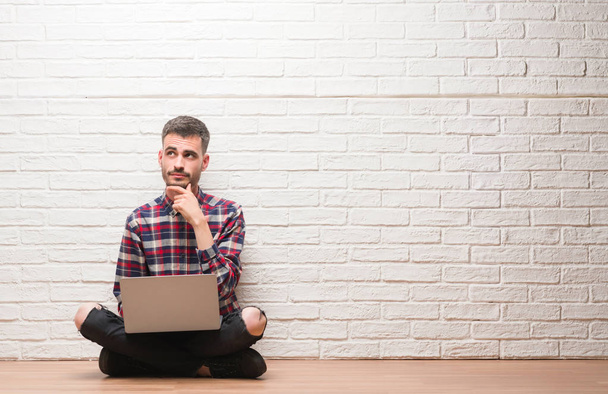 Молодий дорослий чоловік над цегляною стіною, використовуючи ноутбук серйозне обличчя, думаючи про питання, дуже заплутана ідея
 - Фото, зображення