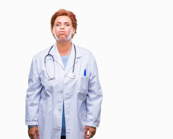 Vedoucí lékař Kavkazský žena nosí zdravotní uniformu izolované pozadí nafoukla tváře s legrační obličej. Ústa naplněny vzduchem, šílený výraz. - Fotografie, Obrázek