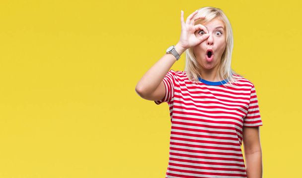 Young beautiful blonde woman over isolated background doing ok gesture shocked with surprised face, eye looking through fingers. Unbelieving expression. - Photo, Image
