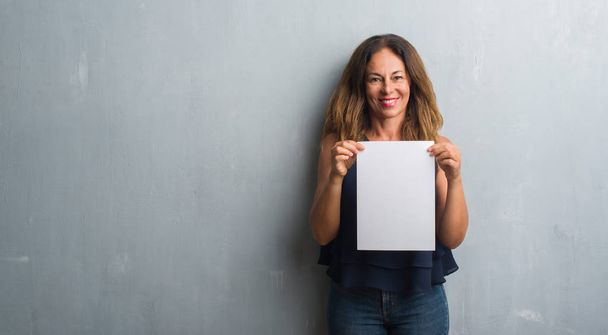 Middle age hispanic woman holding bank paper sheet with a happy face standing and smiling with a confident smile showing teeth - Фото, изображение