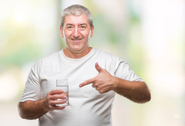 Красивый пожилой человек, пьющий стакан воды на изолированном фоне, очень доволен, указывая рукой и пальцем.
 - Фото, изображение
