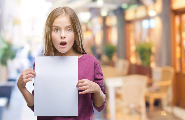 Young beautiful girl holding blank sheet paper over isolated background scared in shock with a surprise face, afraid and excited with fear expression - Valokuva, kuva