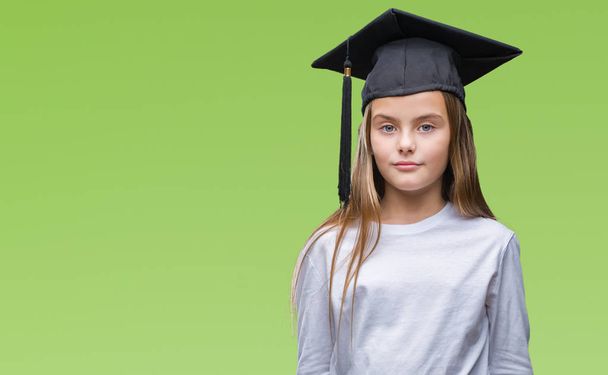 Young beautiful girl wearing graduate cap over isolated background with serious expression on face. Simple and natural looking at the camera. - Photo, Image
