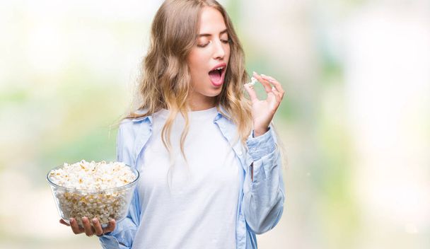 Красива молода блондинка їсть попкорн над ізольованим тлом з впевненим виразом на розумне обличчя думаючи серйозно
 - Фото, зображення