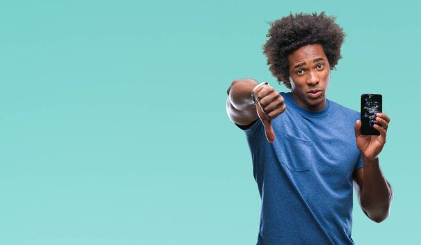Афро-американец держит сломанный смартфон на изолированном фоне с сердитым лицом, негативный знак, показывающий неприязнь с опущенными пальцами, концепция отказа
 - Фото, изображение