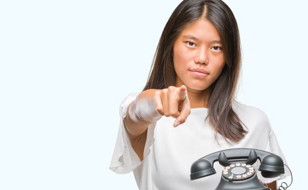 Jeune femme asiatique tenant téléphone vintagera sur fond isolé pointant du doigt la caméra et à vous, signe de la main, geste positif et confiant de l'avant
 - Photo, image