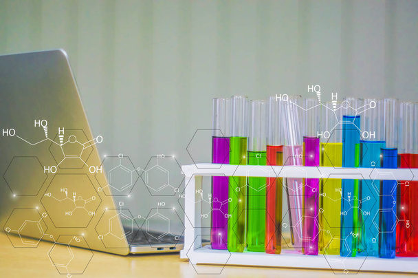 Colorido recipiente de vidrio colocado cerca de un ordenador portátil en el laboratorio y un icono químico. Con el concepto de investigación e invención de nuevos productos y medicamentos para los seres humanos en el futuro
. - Foto, imagen