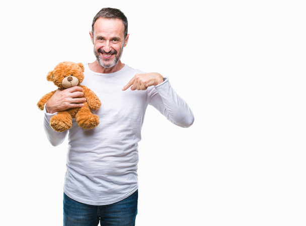 Middle age senior hoary man holding teddy bear over isolated background with surprise face pointing finger to himself - Valokuva, kuva