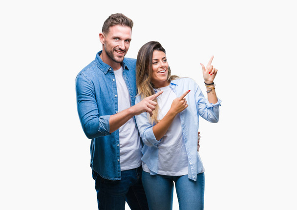 Νεαρό ζευγάρι στην αγάπη πέρα από το απομονωμένο υπόβαθρο χαμογελώντας και εξετάζοντας τη φωτογραφική μηχανή κατάδειξης με δύο χέρια και τα δάχτυλα στο πλάι. - Φωτογραφία, εικόνα