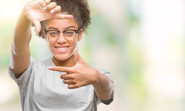 若いアフロのアメリカ人の女性は笑顔と幸せそうな顔で指手作りフレーム分離の背景にメガネを着用します。創造性と写真のコンセプト. - 写真・画像