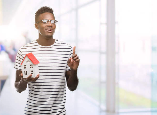 Joven afroamericano hombre sosteniendo casa sorprendido con una idea o pregunta señalando el dedo con la cara feliz, número uno
 - Foto, imagen