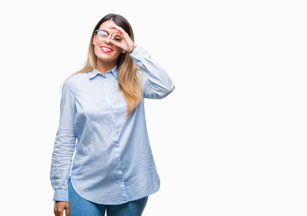 Young beautiful business woman wearing glasses over isolated background doing ok gesture with hand smiling, eye looking through fingers with happy face. - Foto, Imagem