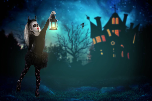 Halloween, holidays, masquerade concept - the portrait of young little beautiful girl with skull makeup holding a lamp. Halloween, face-art, skull make up concept. girl looking smth in the dark against the backdrop of a scary fairytale house in the f - Foto, Imagem