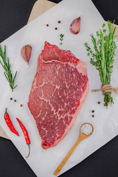 Creative Top view flat lay of fresh raw beef meat striploin steak with rosemary thyme herbs garlic pepper mushrooms on black background with copy space. Food preparation cooking concept - Zdjęcie, obraz
