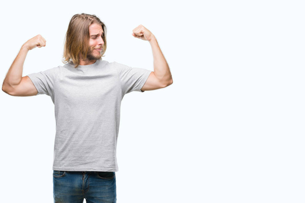 Jeune homme beau aux cheveux longs sur fond isolé montrant les muscles des bras souriant fier. Concept de fitness
. - Photo, image