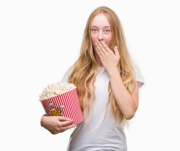 Kobieta blonde nastolatek jedzenia kukurydza pop pokrywa usta ręką szoku ze wstydem za błąd, wyrażenie strachu, boi się w milczeniu, tajne koncepcja - Zdjęcie, obraz