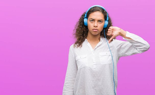 Young hispanic woman wearing headphones with angry face, negative sign showing dislike with thumbs down, rejection concept - Foto, immagini