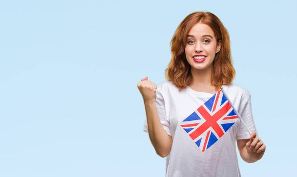 Jonge mooie vrouw houdt van vlag van het Verenigd Koninkrijk over geïsoleerde achtergrond schreeuwen trots en vieren overwinning en succes erg enthousiast, juichende van emotie - Foto, afbeelding