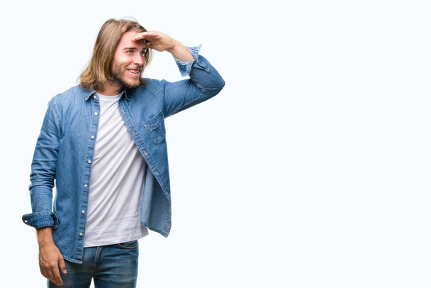 Young handsome man with long hair over isolated background very happy and smiling looking far away with hand over head. Searching concept. - Foto, Imagen