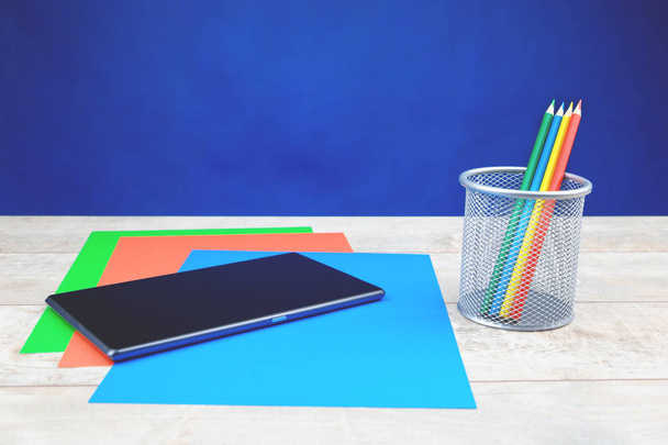 Kolorowe kredki i arkuszy papieru na białe drewniane biurka, tablet i ciemnym niebieskim tle - Zdjęcie, obraz