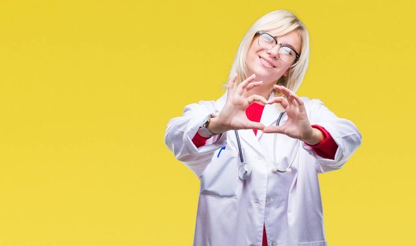 Młoda piękna Blondynka lekarz kobieta ubrana uniform medyczny na białym tle uśmiechający się w miłość serce symbol i kształt rękami. Romantyczna koncepcja. - Zdjęcie, obraz