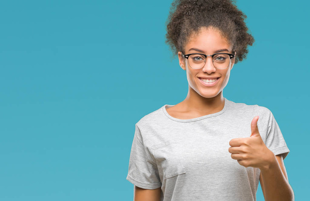 Молодая афро-американка в очках на изолированном фоне делает счастливый жест вверх рукой. Утверждение выражения лица, смотрящего в камеру с успехом
. - Фото, изображение