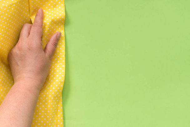 Female hand touching yellow cloth on green background. With copy space. - Фото, зображення