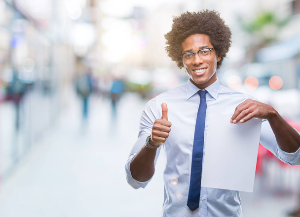Afro american man holding blank paper contract over isolated background happy with big smile doing ok sign, thumb up with fingers, excellent sign - Foto, imagen