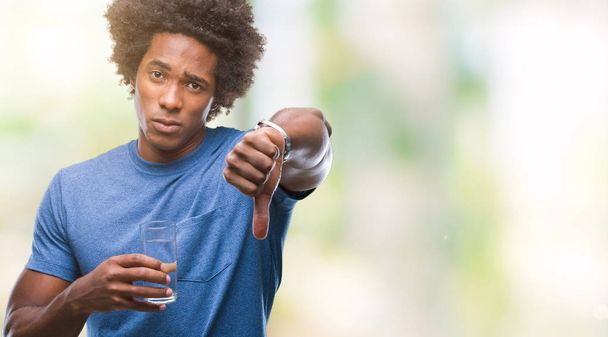 Afro-amerikai ember pohár vizet iszik felett Haragos arc, negatív előjellel mutatja ellenszenv a hüvelykujját lefelé, elutasítás koncepció elszigetelt háttér - Fotó, kép