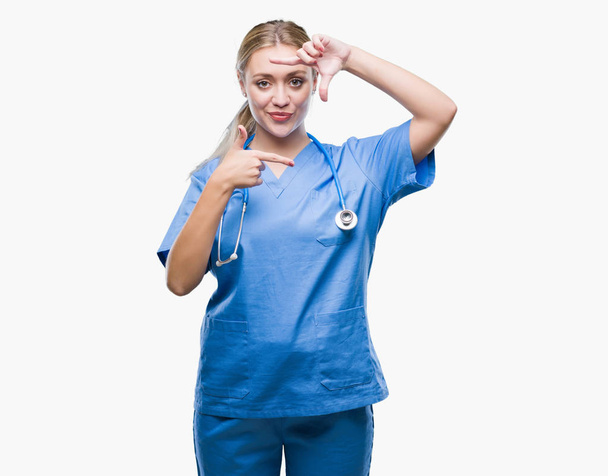 Jonge blonde chirurg dokter vrouw over geïsoleerde achtergrond glimlachend maken frame met handen en vingers met blij gezicht. Creativiteit en fotografie concept. - Foto, afbeelding
