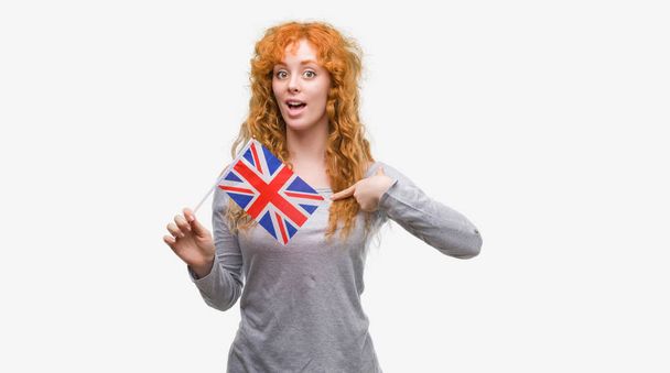 自分自身に驚き顔ポインティング指でイギリスの旗を保持している赤毛の若い女性 - 写真・画像