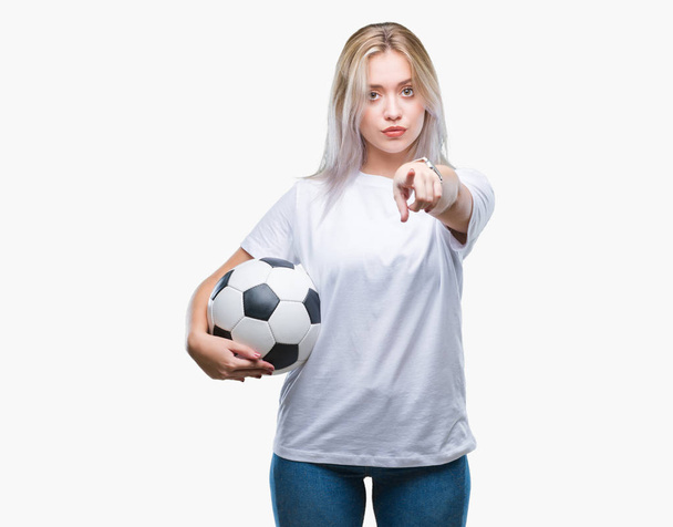 Giovane donna bionda che tiene il pallone da calcio su sfondo isolato puntando con il dito alla fotocamera e a te, segno della mano, gesto positivo e fiducioso dal davanti
 - Foto, immagini