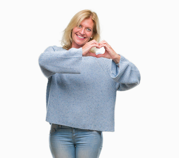 Középkorú szőke nő visel téli pulóver, mosolyogva szerelmes szív szimbólum és a kéz alakú elszigetelt háttérhez képest. Romantikus fogalma. - Fotó, kép