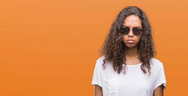 Young hispanic woman wearing sunglasses skeptic and nervous, frowning upset because of problem. Negative person. - 写真・画像