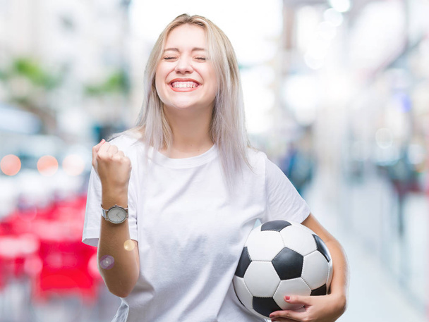 Mladá blond žena držící fotbal fotbalový míč nad izolované pozadí křičí hrdá a slaví vítězství a úspěch, velmi rádi, fandění emoce - Fotografie, Obrázek