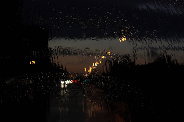 Návrat domů. Bokeh světla, mokré rozmazaný pohled na silniční dopravy v Gatchina na deštivý večer předním oknem autobusu. Dešťové kapky a stopy z domovníků na skleněné okno autobusu. - Fotografie, Obrázek