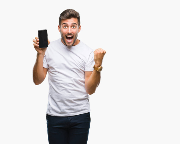 Young handsome man showing smartphone screen over isolated background screaming proud and celebrating victory and success very excited, cheering emotion - Photo, Image