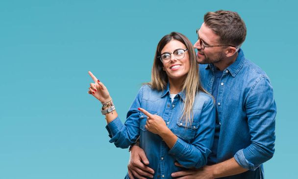 Νεαρό ζευγάρι στην αγάπη φορώντας γυαλιά πέρα από το απομονωμένο υπόβαθρο χαμογελώντας και εξετάζοντας τη φωτογραφική μηχανή κατάδειξης με δύο χέρια και τα δάχτυλα στο πλάι. - Φωτογραφία, εικόνα