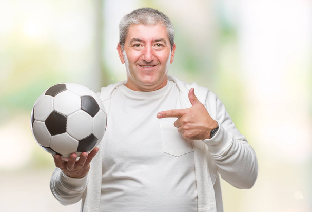 Handsome senior man holding soccer football ball over isolated background very happy pointing with hand and finger - Foto, afbeelding