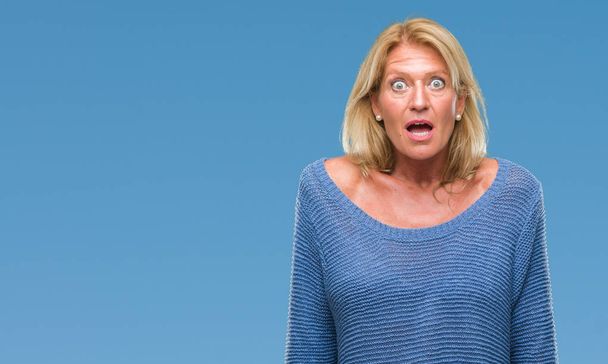 Blonde Frau mittleren Alters trägt Winterpullover über isoliertem Hintergrund, ängstlich und schockiert mit überraschtem Ausdruck, Angst und aufgeregtem Gesicht. - Foto, Bild