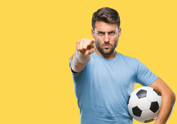 Young handsome man holding soccer football ball over isolated background pointing with finger to the camera and to you, hand sign, positive and confident gesture from the front - Foto, imagen