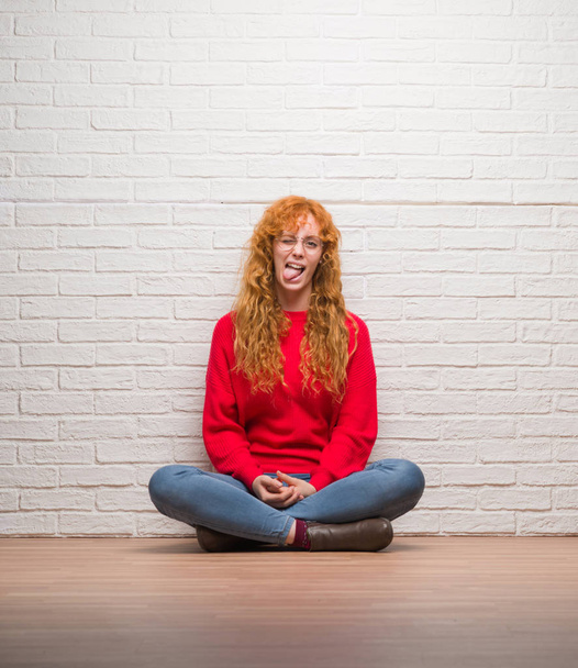 Fiatal vöröshajú nő ül tégla fal ragasztás nyelvét elégedett vicces kifejezés. Érzés-fogalma. - Fotó, kép