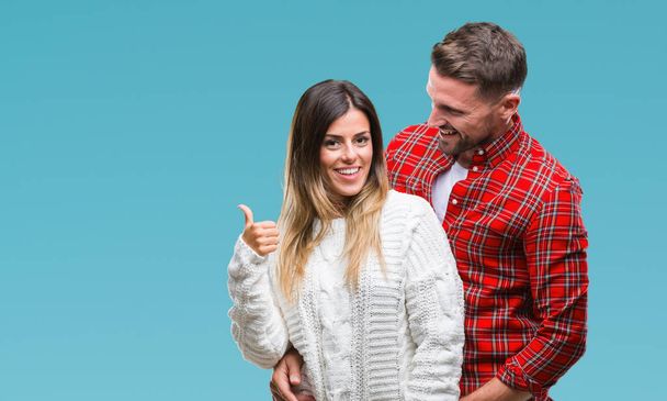 Young couple in love wearing winter sweater over isolated background smiling with happy face looking and pointing to the side with thumb up. - Zdjęcie, obraz