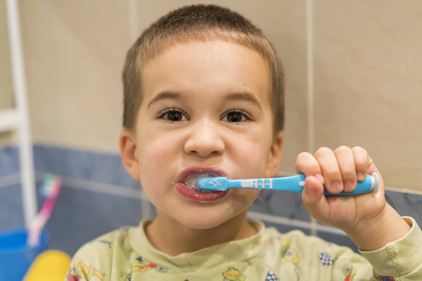 de jongen heeft het borstelen van zijn tanden in de badkamer voor 4 jaar. Close-up. jongetje borstels tanden in een badkamer - Foto, afbeelding