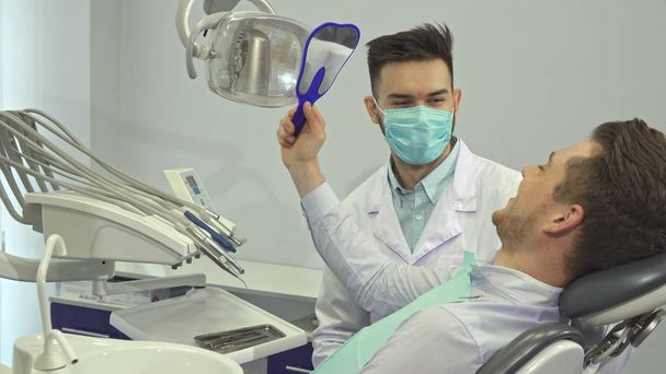Patient blickt in Zahnarztpraxis im Spiegel auf seine Zähne - Foto, Bild