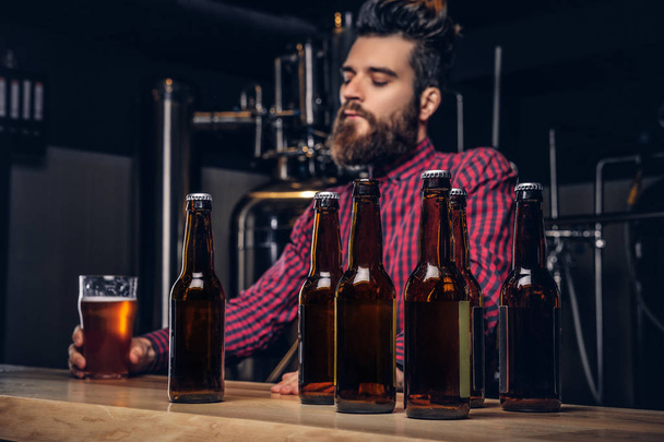 Photo avec des bouteilles de bière artisanale au premier plan et un homme barbu buvant en arrière-plan
. - Photo, image